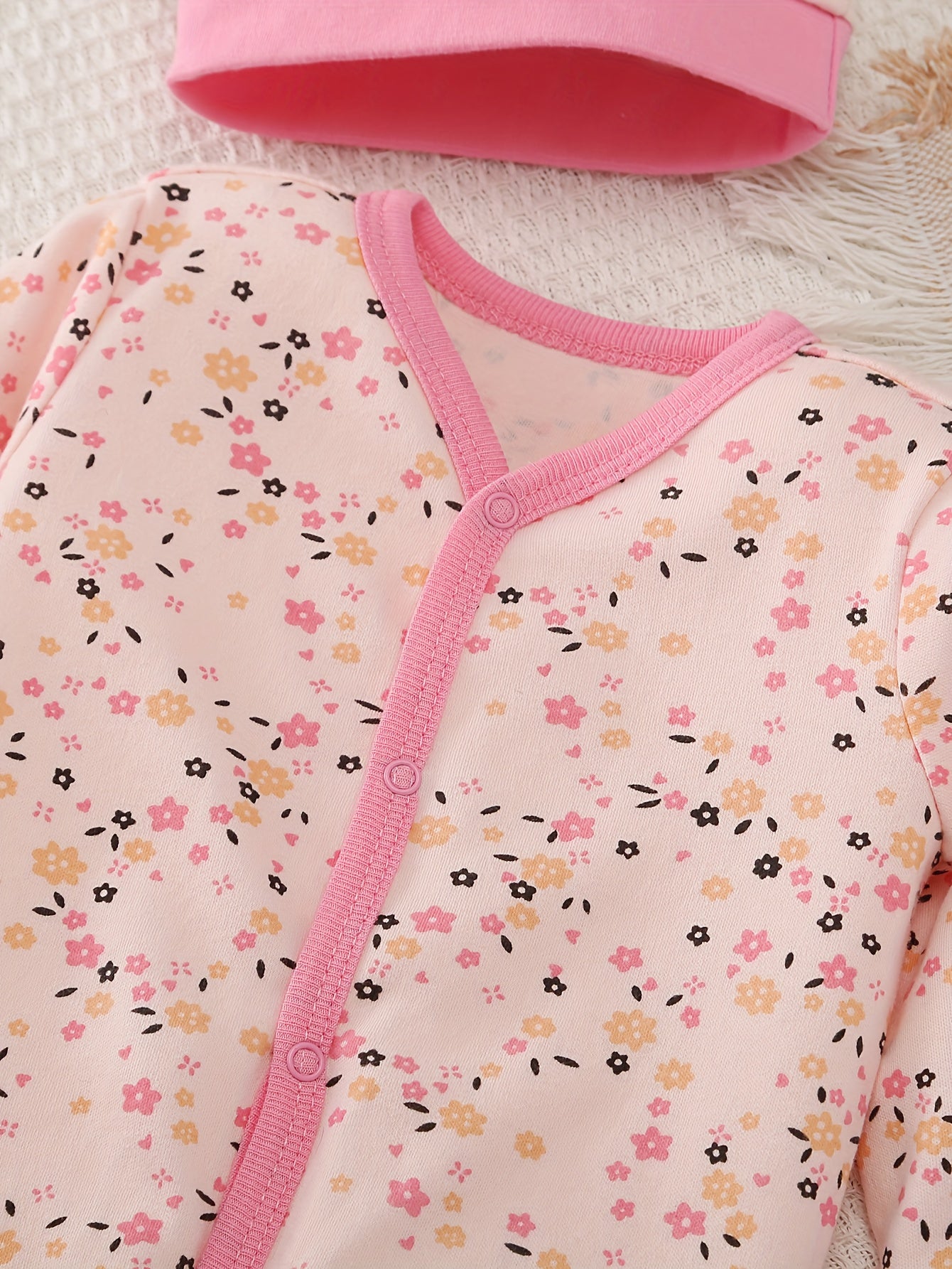 Baby outfit with floral pattern and pink trim on a textured surface