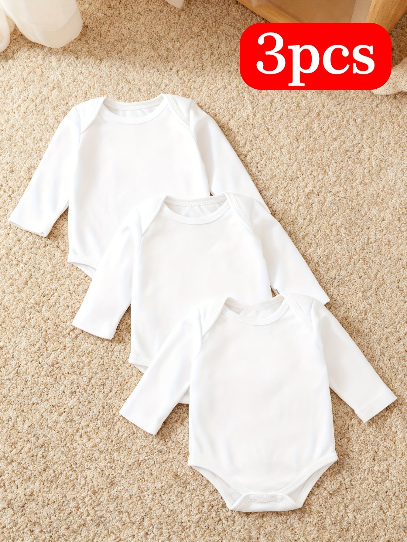 Three white baby bodysuits on a beige carpet with a '3pcs' label.