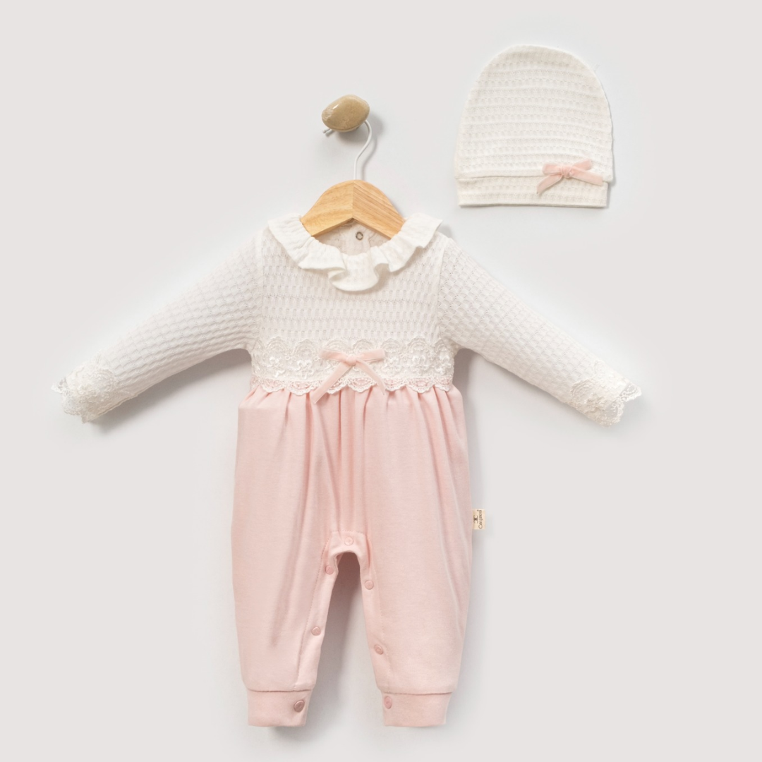 A baby girl's two-piece outfit set consisting of a long-sleeve jumpsuit and a matching knit bonnet. The jumpsuit features a textured cream-white top with a ruffled collar and lace trim, paired with soft pink pants.