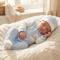 A sleeping newborn baby wearing a light blue and white footed onesie with a bear graphic, a matching light blue and white beanie, and a cream cable-knit blanket in a softly lit nursery.