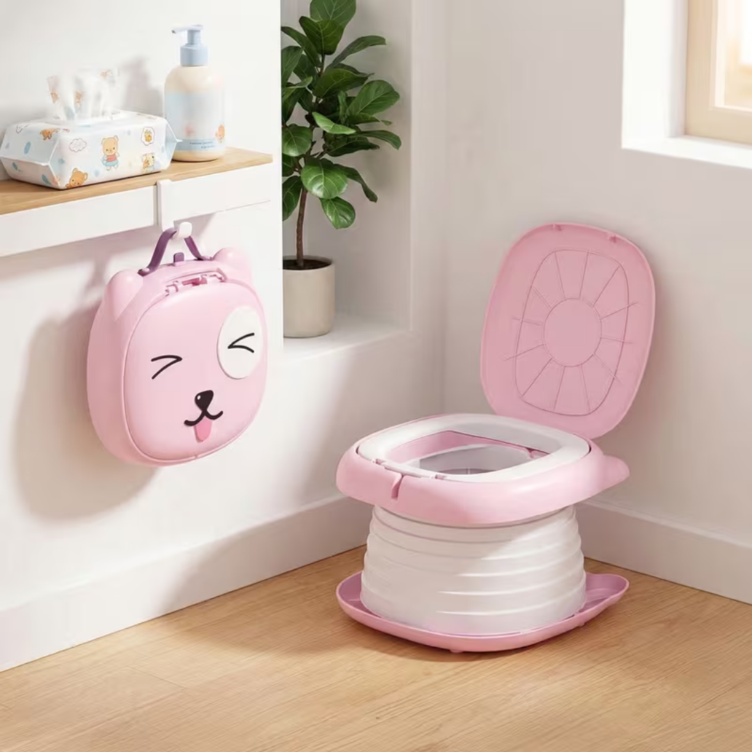 Pink children's potty seat with cartoon face design on a wooden floor.