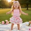 Child in a pink dress with a floral skirt standing on a blanket in a park.