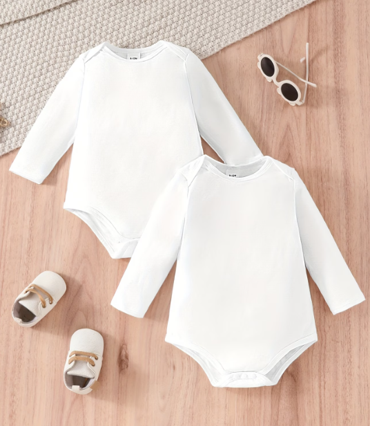 Two white baby bodysuits on a wooden surface with baby shoes and sunglasses.