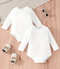 Two white baby bodysuits on a wooden surface with baby shoes and sunglasses.