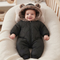 A baby wearing a black quilted snowsuit with a brown faux-fur hood and bear ears, sitting in a cream-colored baby lounger.