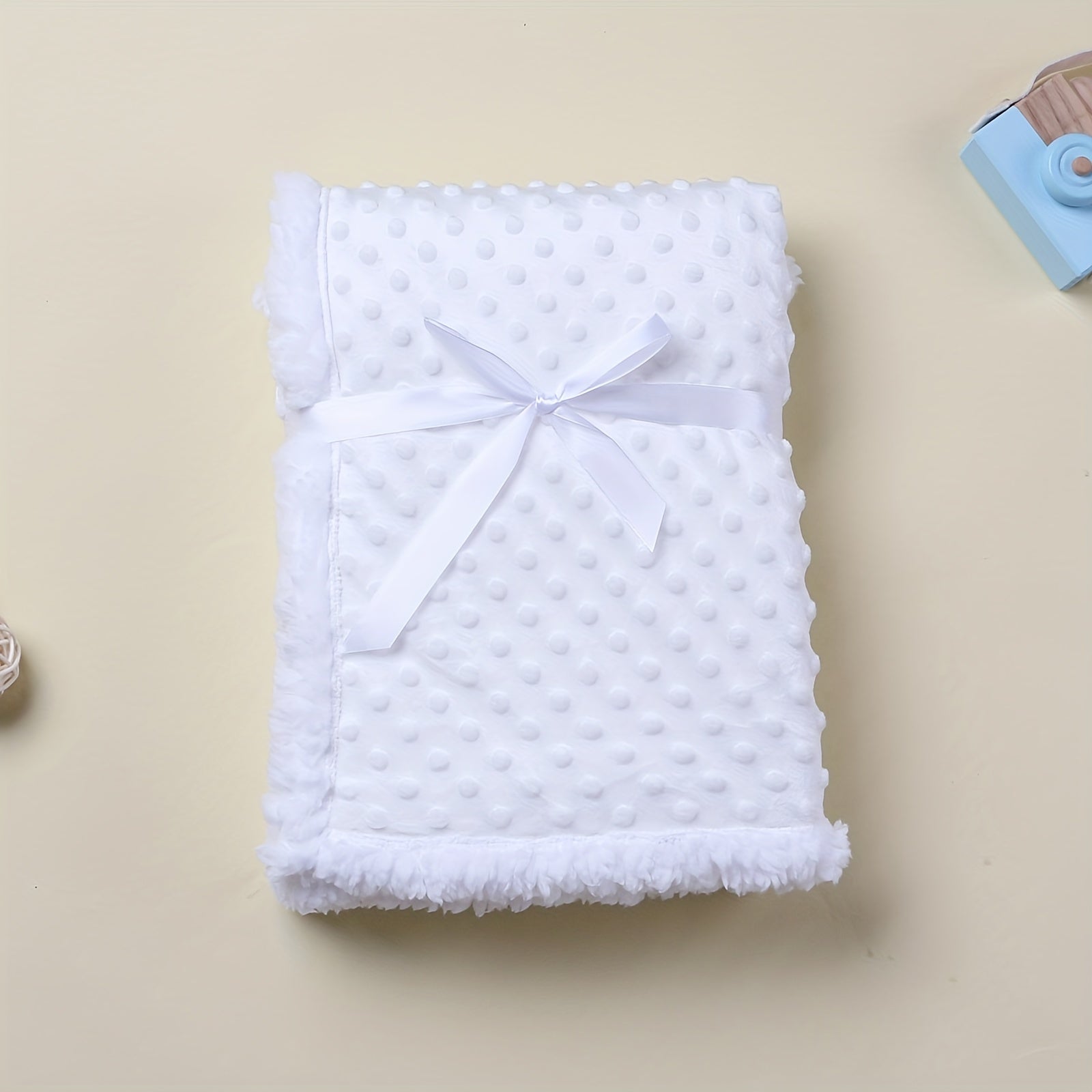 Folded white textured blanket with a bow on a beige background