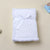 Folded white textured blanket with a bow on a beige background