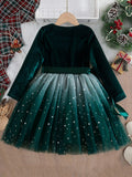 Green velvet dress with star-patterned tulle skirt on a wooden surface with Christmas decorations.