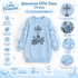 A light blue long-sleeve children's dress with a large embroidered Eiffel Tower motif on the front, surrounded by decorative bows and tulle overlay details. The image is a product information graphic with multiple callout circles and text listing features such as rhinestone eiffel tower, embroidered rose details, tulle sleeve overlay, satin bow accents, and ribbed cuffs and hem.
