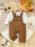 Children's outfit with brown overalls and white shirt with bear pattern on a wooden floor.
