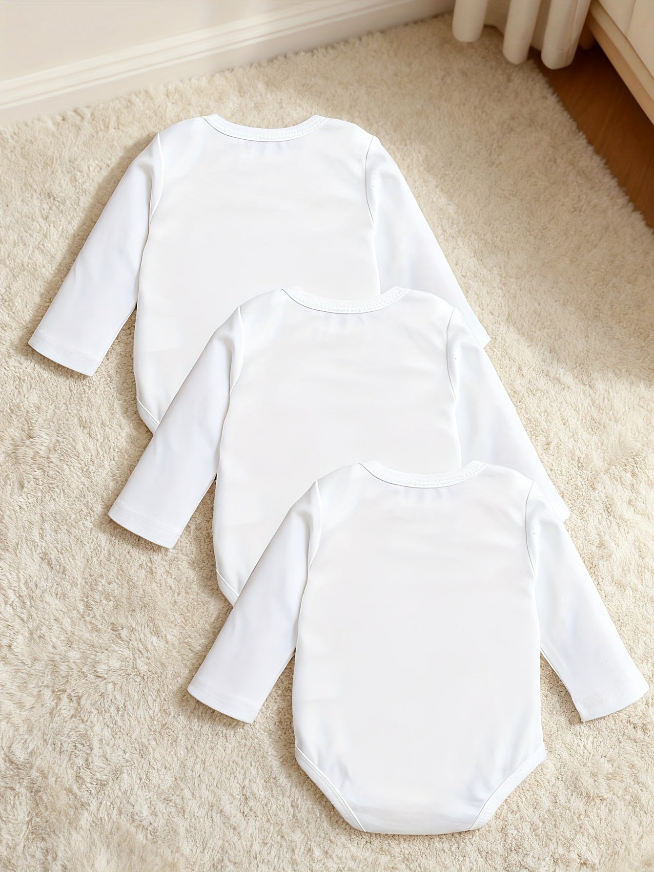 Three white baby bodysuits on a beige carpet