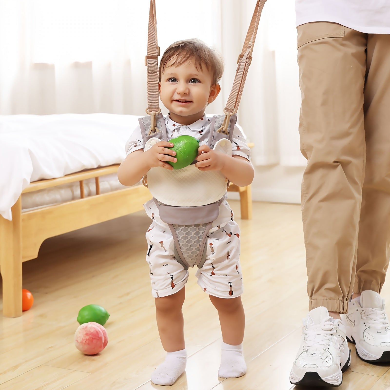 Child standing in a room holding a green toy, with a bed and toys in the background.