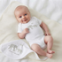 A smiling baby lying on a cream blanket, wearing a short-sleeve white bodysuit with a gray elephant print and the text 'welcome to the world' next to a matching blanket.