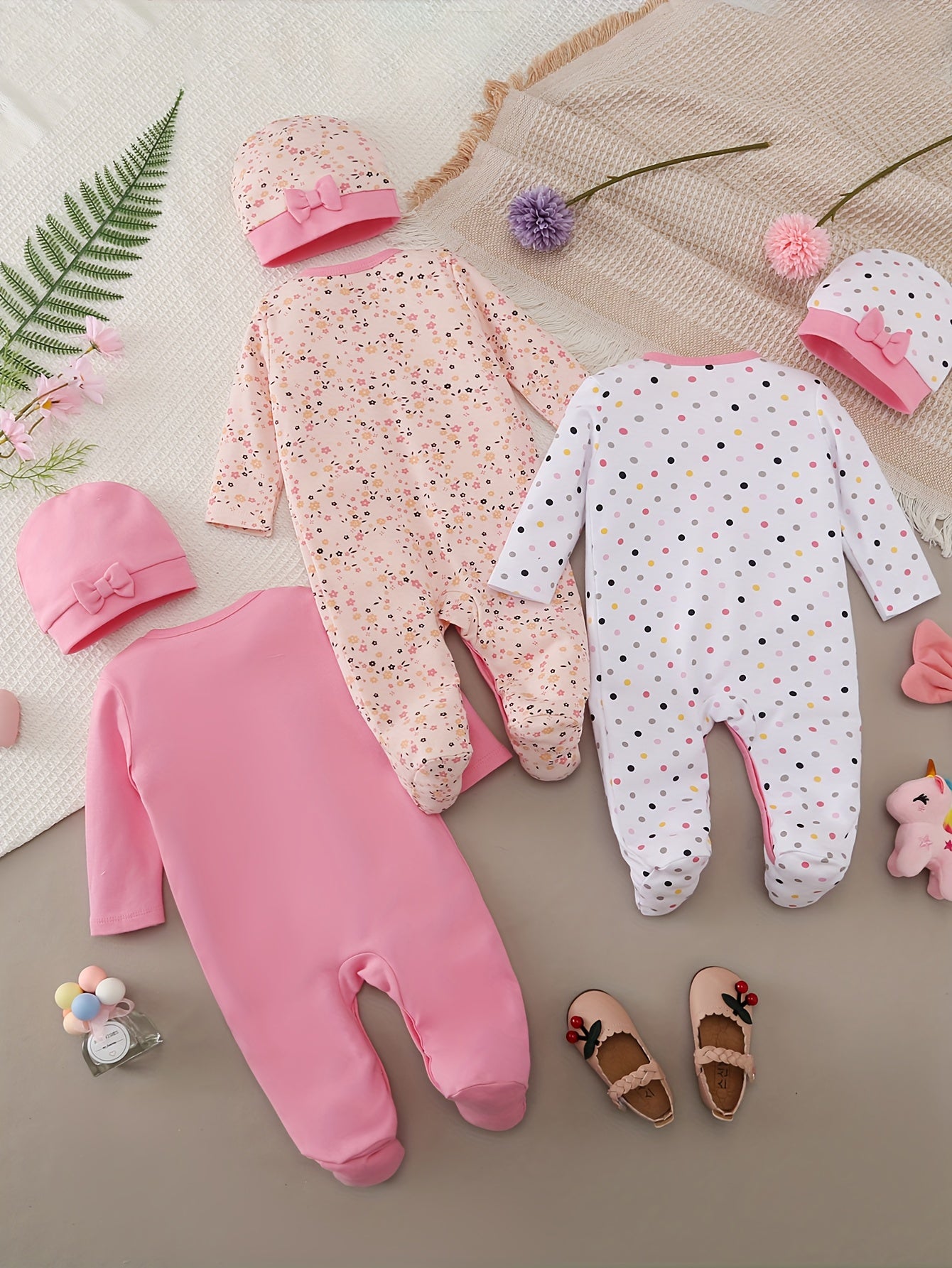 Collection of baby clothing including pink and white onesies with matching hats and shoes on a textured surface.