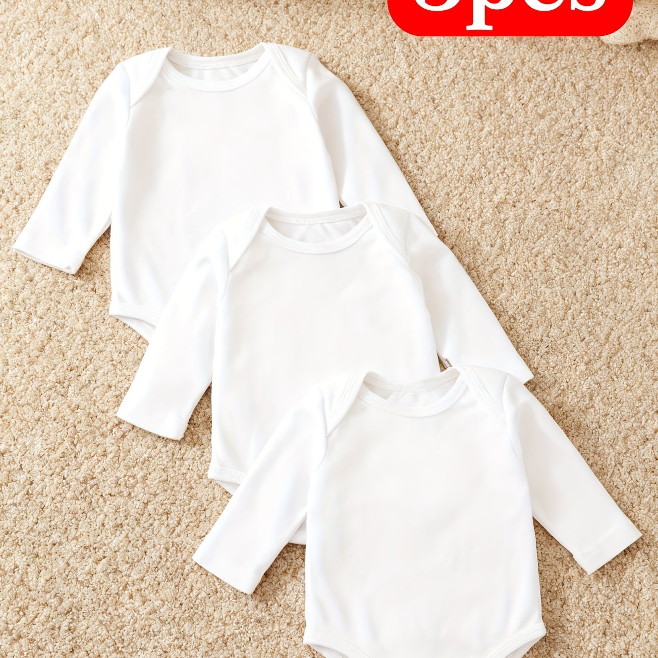 Three white baby onesies on a beige carpet with a red 'Opes' label.