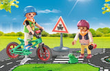 Playmobil figures of children with bicycles and a traffic sign in a park setting