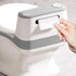 Hand using a white and gray paper towel dispenser on a light wooden surface