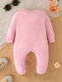Pink baby onesie on a wooden surface with sunglasses and flowers in the background