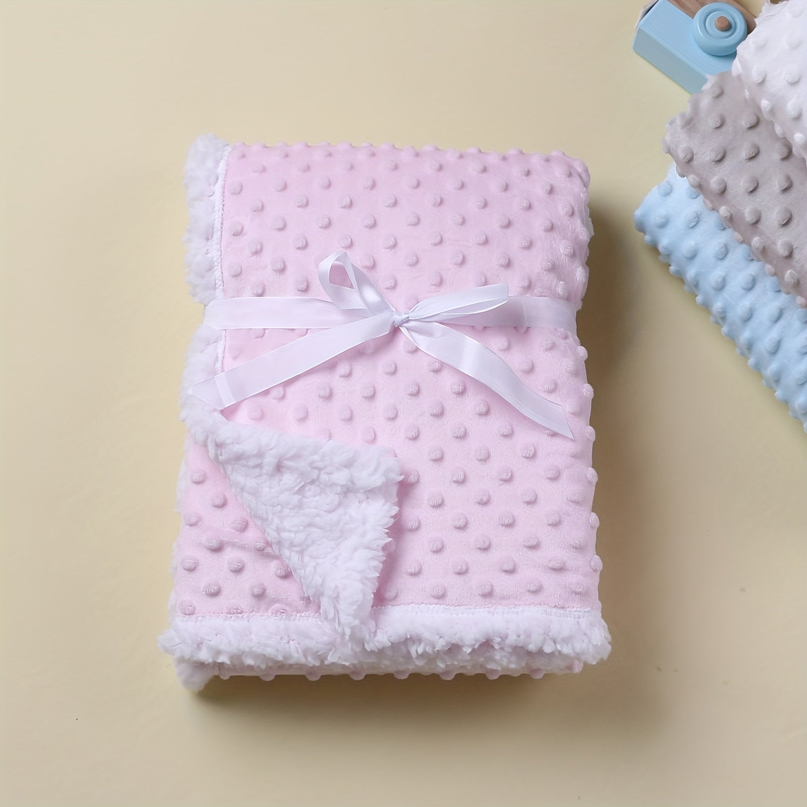 Pink baby blanket with white trim and bow on a beige background