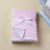 Pink baby blanket with white trim and bow on a beige background