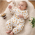 Baby in a floral onesie lying on a soft surface with flowers and a basket in the background.
