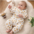 Baby in a floral onesie lying on a soft surface with flowers and a basket in the background.