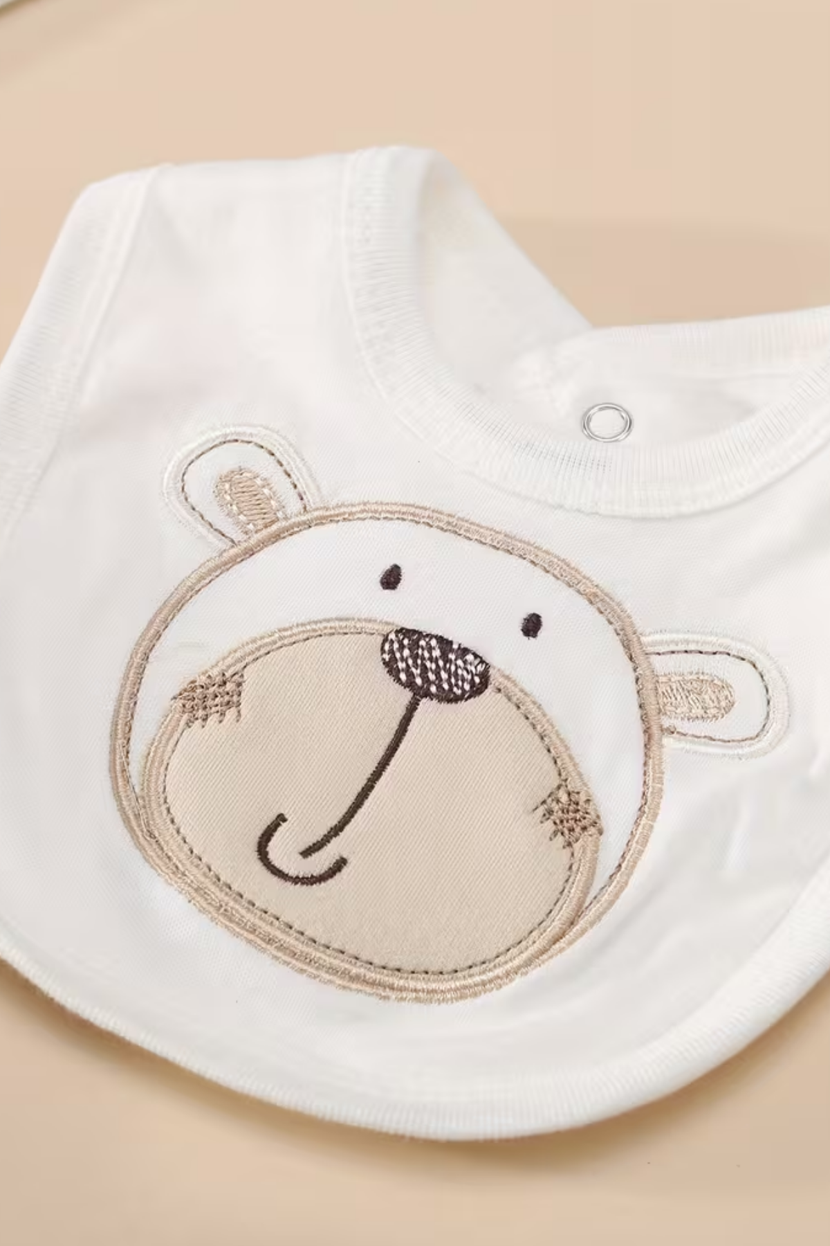 White baby bib with embroidered bear face design on a beige background