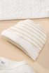 Folded white fabric with gold stripes on a beige surface
