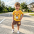 Child wearing a yellow t-shirt with a tiger design and brown shorts standing on a street.