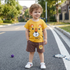 Child wearing a yellow t-shirt with a tiger design and brown shorts standing on a road.