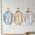 Three baby bodysuits on hangers against a white wall.