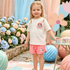Young girl in a Minnie Mouse outfit standing in a colorful outdoor setting with flowers and balloons.