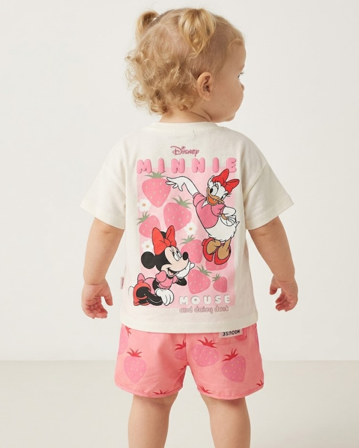 Child wearing a Disney Minnie Mouse outfit with a white t-shirt and pink shorts on a plain background