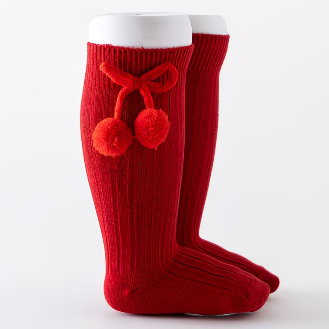 Red knee-high socks with pom-poms and a bow on a white background