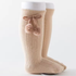 Beige knee-high socks with a bow and pom-pom detail on a white background