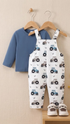 Children's blue shirt and white overalls with tractor pattern on a beige wall background