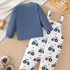Children's blue long-sleeve shirt and white pants with tractor pattern on a beige carpet.