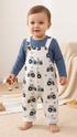 Baby wearing a blue long-sleeve shirt and white overalls with tractor pattern on a light background