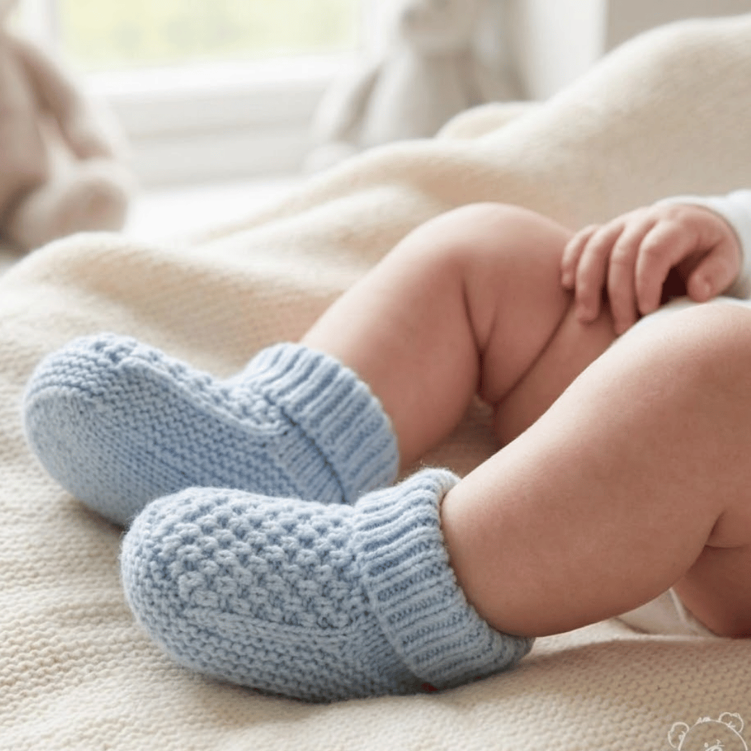 Baby's feet wearing blue knitted booties on a soft surface