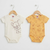Two baby short-sleeve bodysuits hanging on wooden hangers against a plain white wall. The left bodysuit is cream with a brown cartoon mouse drawing and the words 'laughing love.