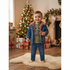 A toddler stands barefoot on a white faux-fur rug in a decorated holiday room, wearing a blue denim jacket with a brown faux-fur collar over an olive green graphic t-shirt and matching blue jeans.