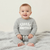 A baby sitting on a soft gray blanket wearing a heather gray sweatshirt and matching pants with 'Little Brother' printed in white across the chest.