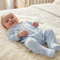 A baby lying on a white faux fur blanket on a bed, wearing a light blue footed sleeper with a white embroidered chest panel.