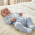 A baby lying on a white faux fur blanket on a bed, wearing a light blue footed sleeper with a white embroidered chest panel.