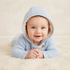 A baby two-piece sweatshirt and jogger pants set in solid white, laid flat on a white faux fur background with decorative props including cotton bolls, a plush toy, and baby shoes.