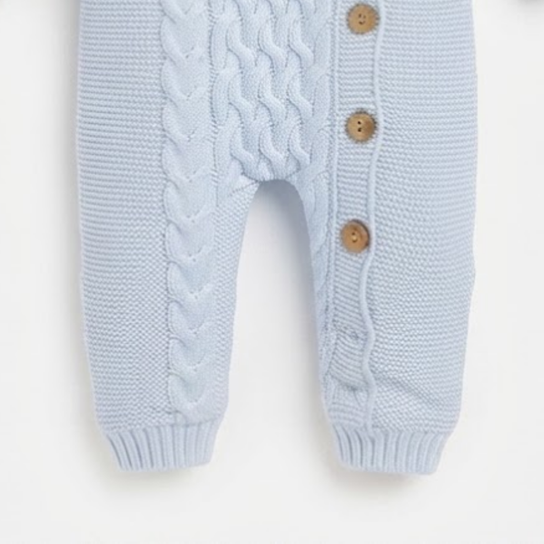 Light blue knit baby romper with cable and braid patterns, featuring three brown wooden buttons on the side.
