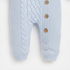 Light blue knit baby romper with cable and braid patterns, featuring three brown wooden buttons on the side.