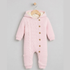A light pink knit hooded baby jumpsuit with a cable-knit front panel, wooden buttons, and a cream-colored fleece lining inside the hood, hanging on a wooden hanger against a light gray background.