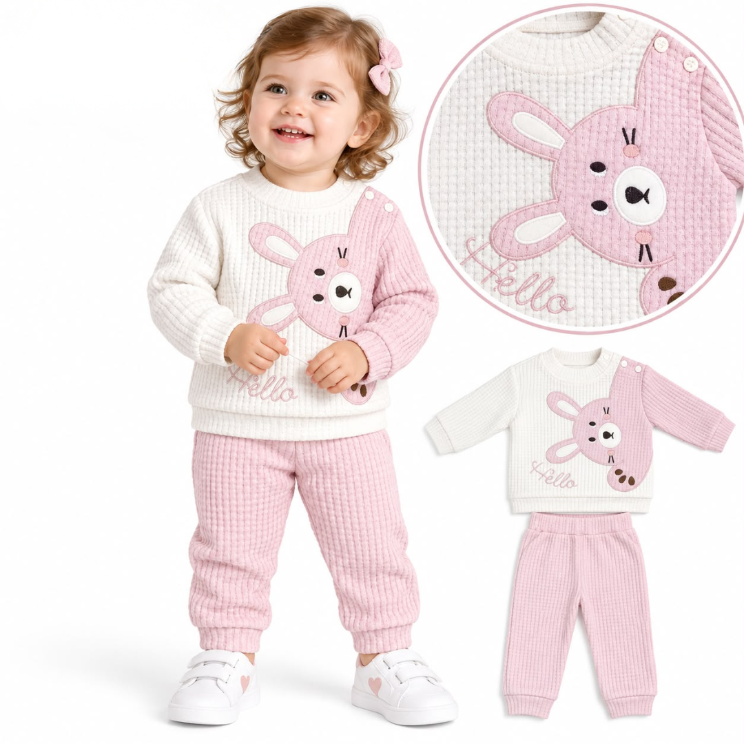 A toddler modeling a two-piece waffle-knit sweatsuit set with a pink bunny applique and 'Hello' text on a cream top and pink pants. A circular inset shows a close-up of the bunny detail, and a smaller standalone view of the outfit appears on the right, all on a white background.