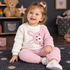 A toddler girl sitting on a dark rug in a cozy room, wearing a waffle-knit two-piece pajama set with a white top featuring a pink bunny graphic and matching pink pants.